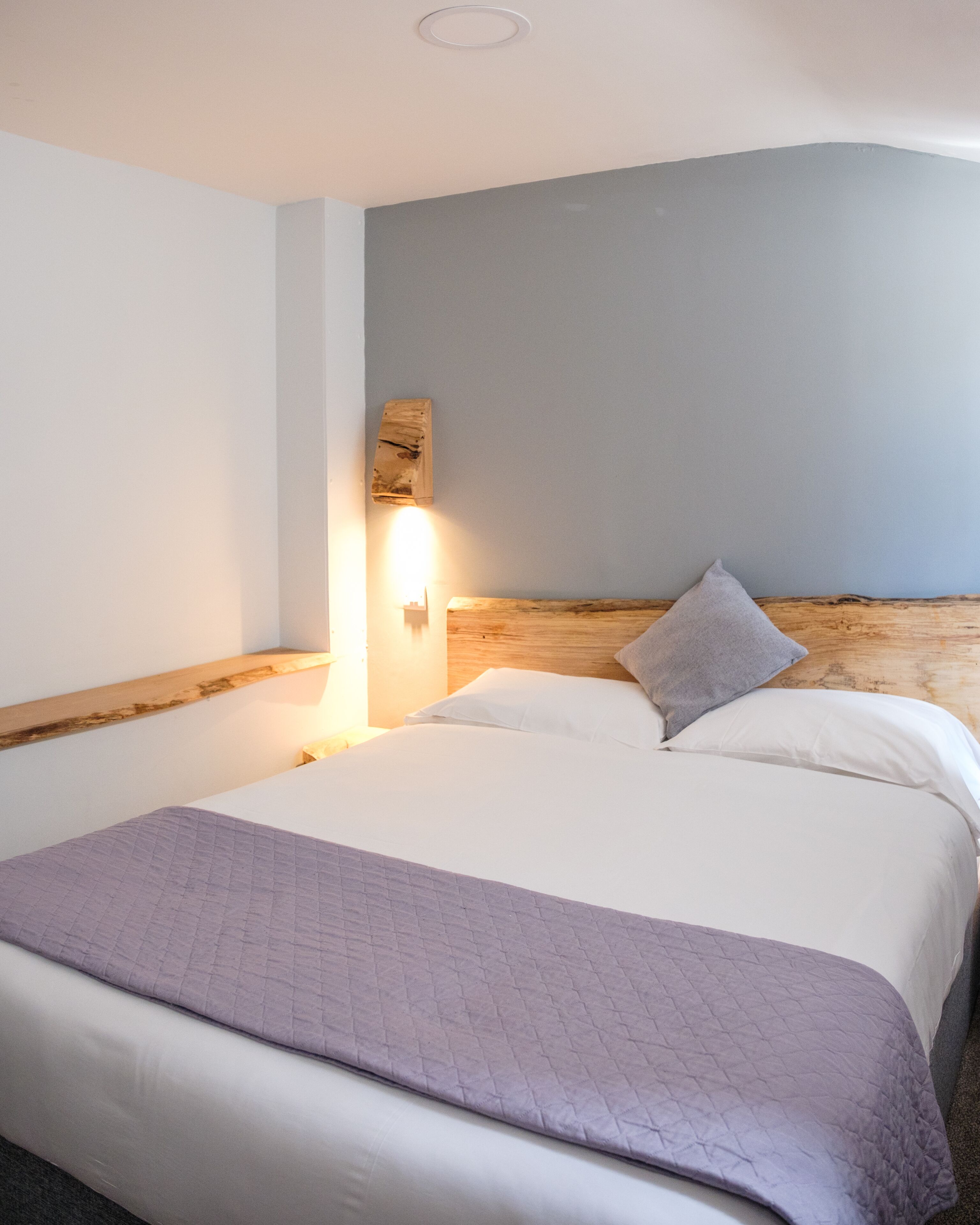 A neatly made bed with a wooden headboard, a bedside lamp, and a wall-mounted light fixture.