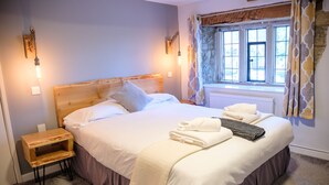 A neatly made bed with pillows and a folded towel, a bedside table, and a window with curtains.