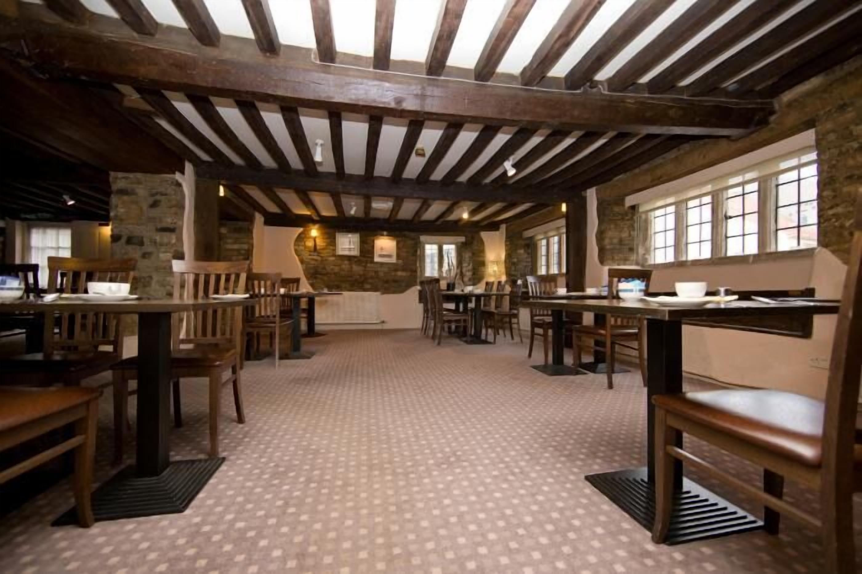 Un restaurant avec des tables et des chaises en bois, des murs en pierre et un sol à motifs.