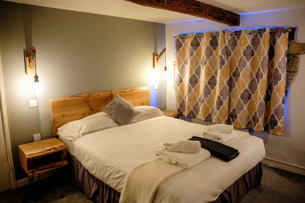 A neatly made bed with pillows and a blanket, a wooden nightstand, and a wall-mounted light fixture.