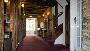 A hallway with a wooden staircase, stone walls, and a red carpet.