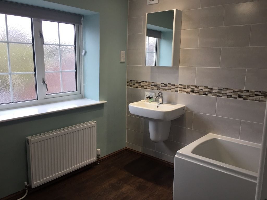 A bathroom with a window, a sink, a mirror, and a bathtub.