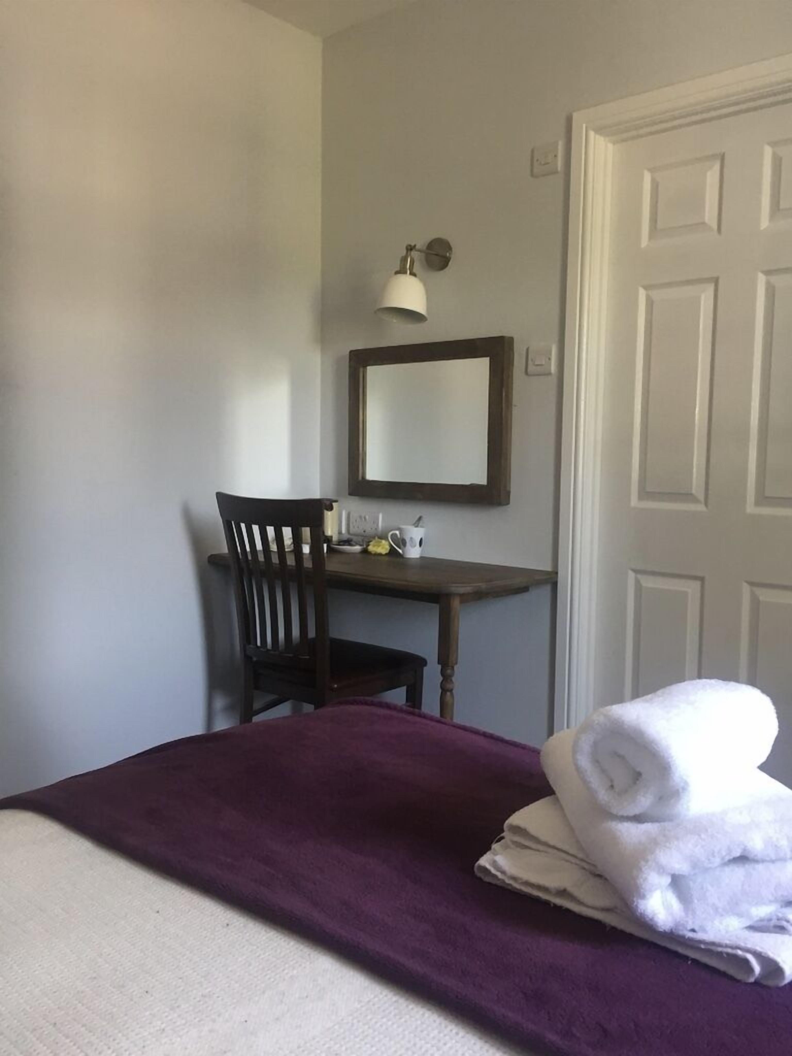 Ein Zimmer mit einem Bett, einem Sessel, einem kleinen Tisch, einem Spiegel und einer Tür.