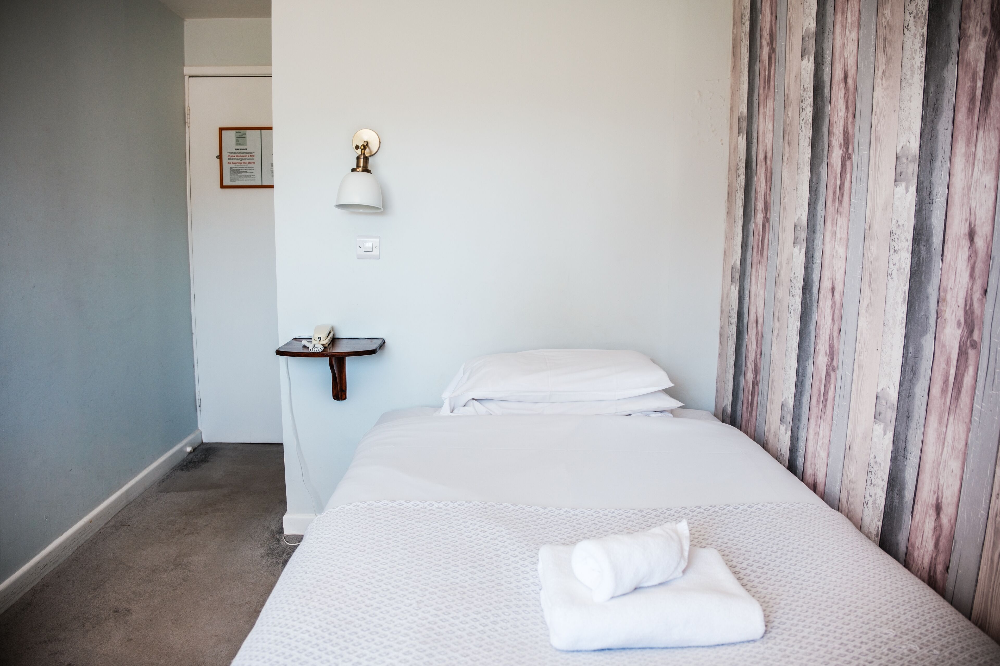 Habitación de hotel con cama, mesita de noche, lámpara de pared y pared revestida de madera.