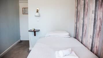 A hotel room with a bed, a small bedside table, a wall-mounted lamp, and a wooden panel wall.