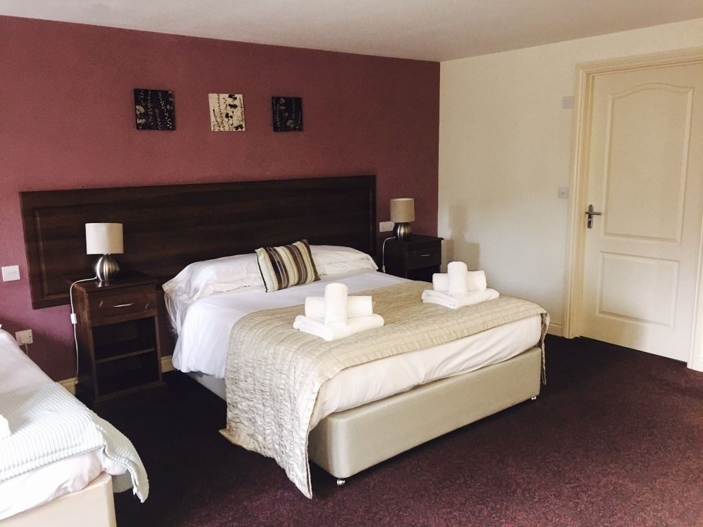 Habitación de hotel con una cama grande, dos mesitas de noche con lámparas, una puerta y una pared con tres cuadros enmarcados.