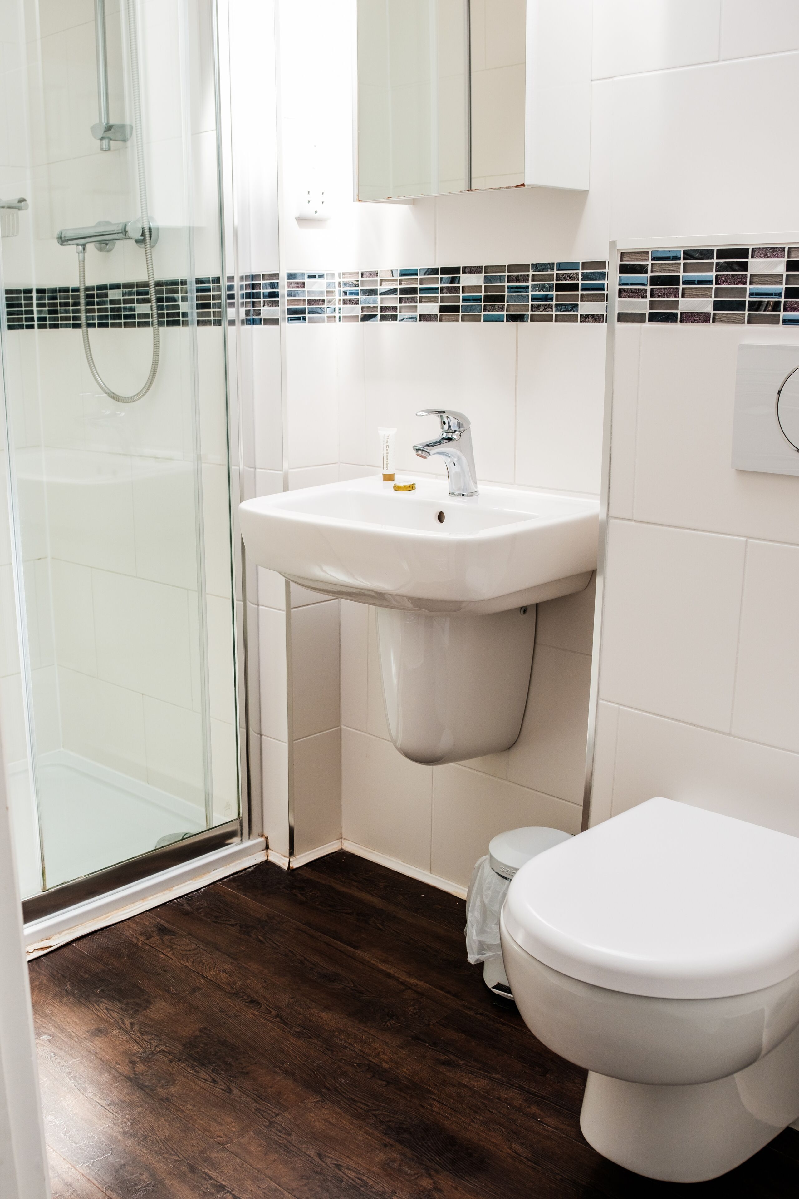Un baño con cabina de ducha de vidrio, un lavamanos blanco con grifo cromado y un inodoro blanco.