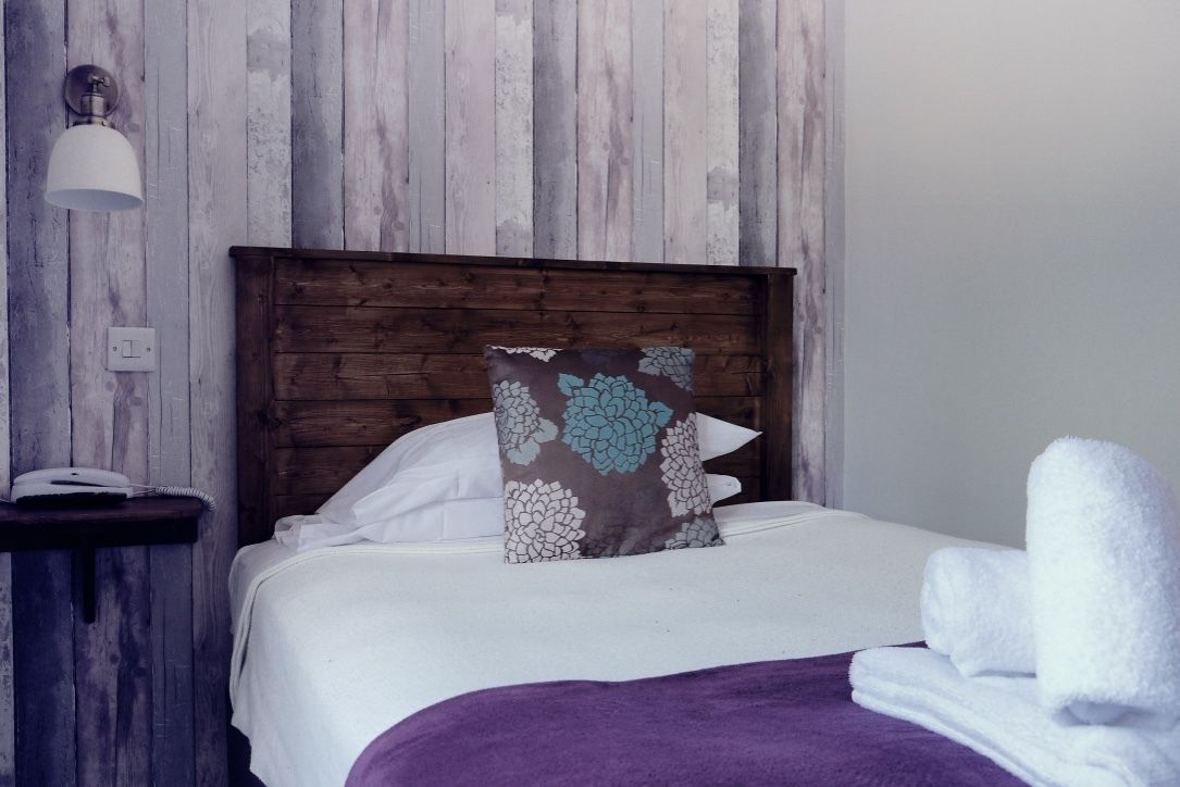 A neatly made bed with a wooden headboard, a decorative pillow, and a purple throw blanket.