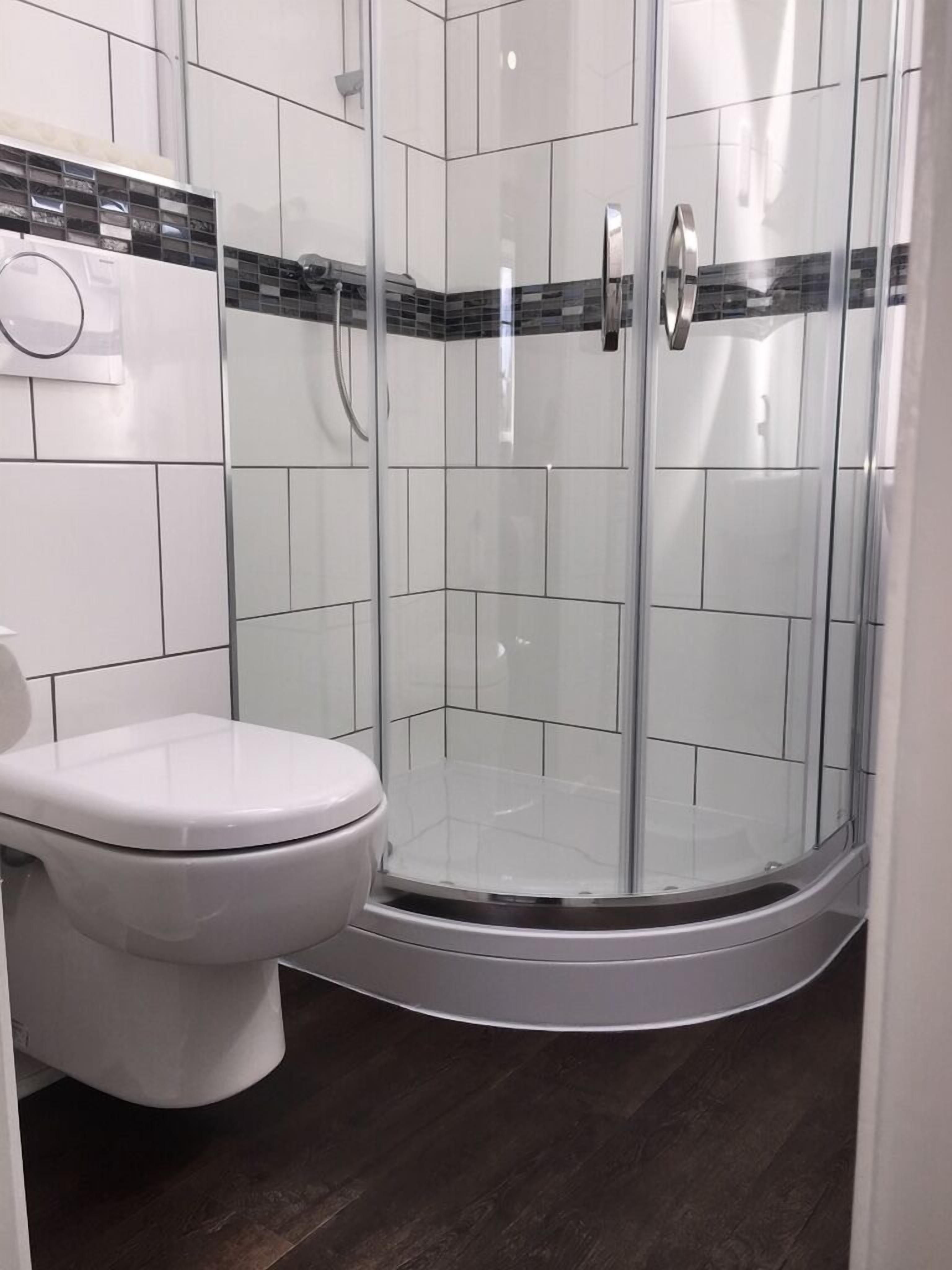Un baño moderno con ducha envuelta en cristal, azulejos blancos y un inodoro.
