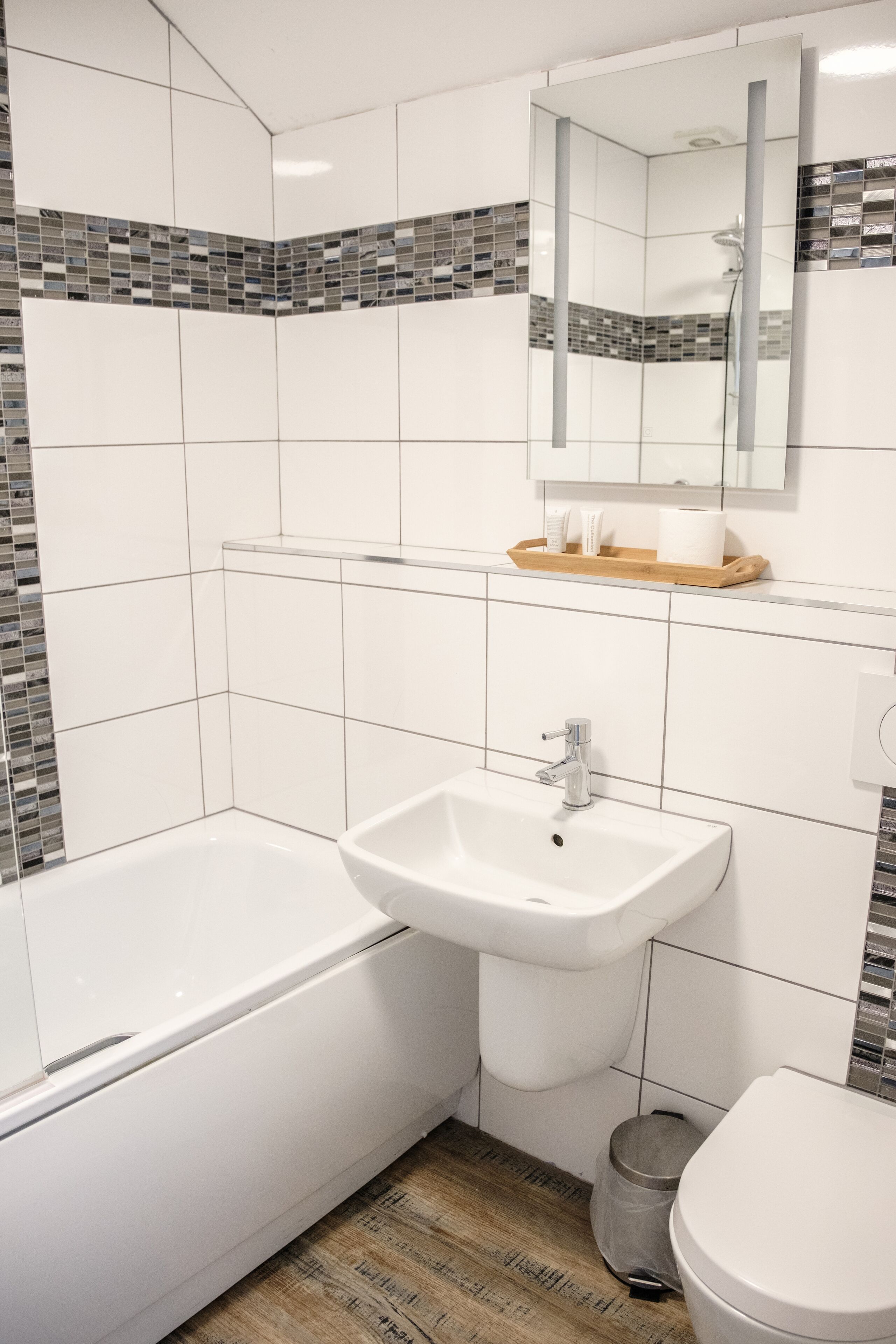 A bathroom with a white sink, a bathtub, and a toilet. There is a mirror above the sink and a shelf with toiletries.