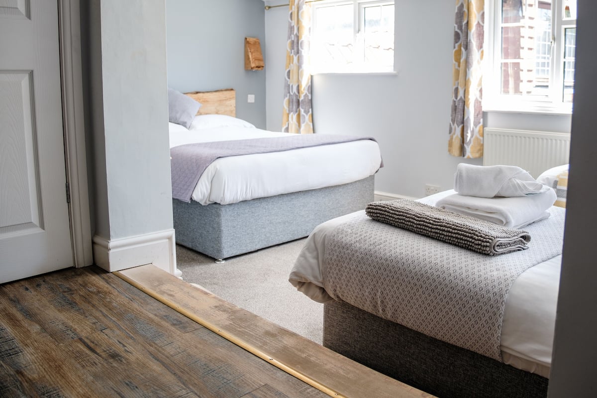 A bedroom with two beds, a wooden floor, and a window with curtains.
