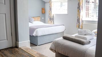 Un dormitorio con dos camas, suelo de madera y una ventana con cortinas.