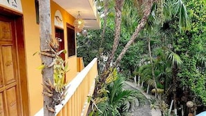 Un étroit sentier bordé d’une végétation luxuriante et un bâtiment jaune doté de portes en bois et d’un balcon.