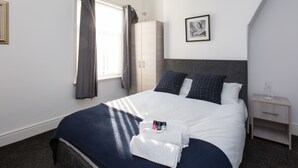 Een keurig opgemaakt slaapkamer met een bed, nachtkastje, kledingkast en een ingelijst schilderij aan de muur.