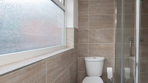Een badkamer met een toilet, een douchecabine van glas en een raam met gezandstraald glas.