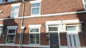 A red brick terraced house with white-framed windows, a grey door, and a white front door.