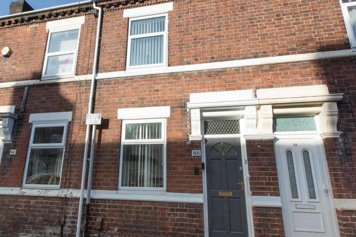 A red brick terraced house with white-framed windows, a grey door, and a white front door.
