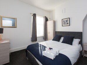 A hotel room with a bed, a desk with a lamp, a wardrobe, and a window with curtains.