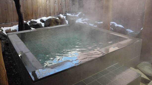 A hot tub surrounded by a wooden fence and rocks, with snow on the ground. - KKR Kawayu (Teshikaga)