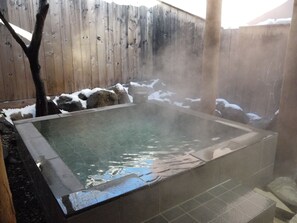 A hot tub surrounded by a wooden fence and rocks, with snow on the ground.
