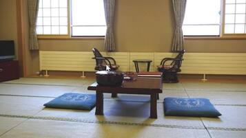A tatami mat room with a low table, two cushions, a small table with a bowl, and a chair.