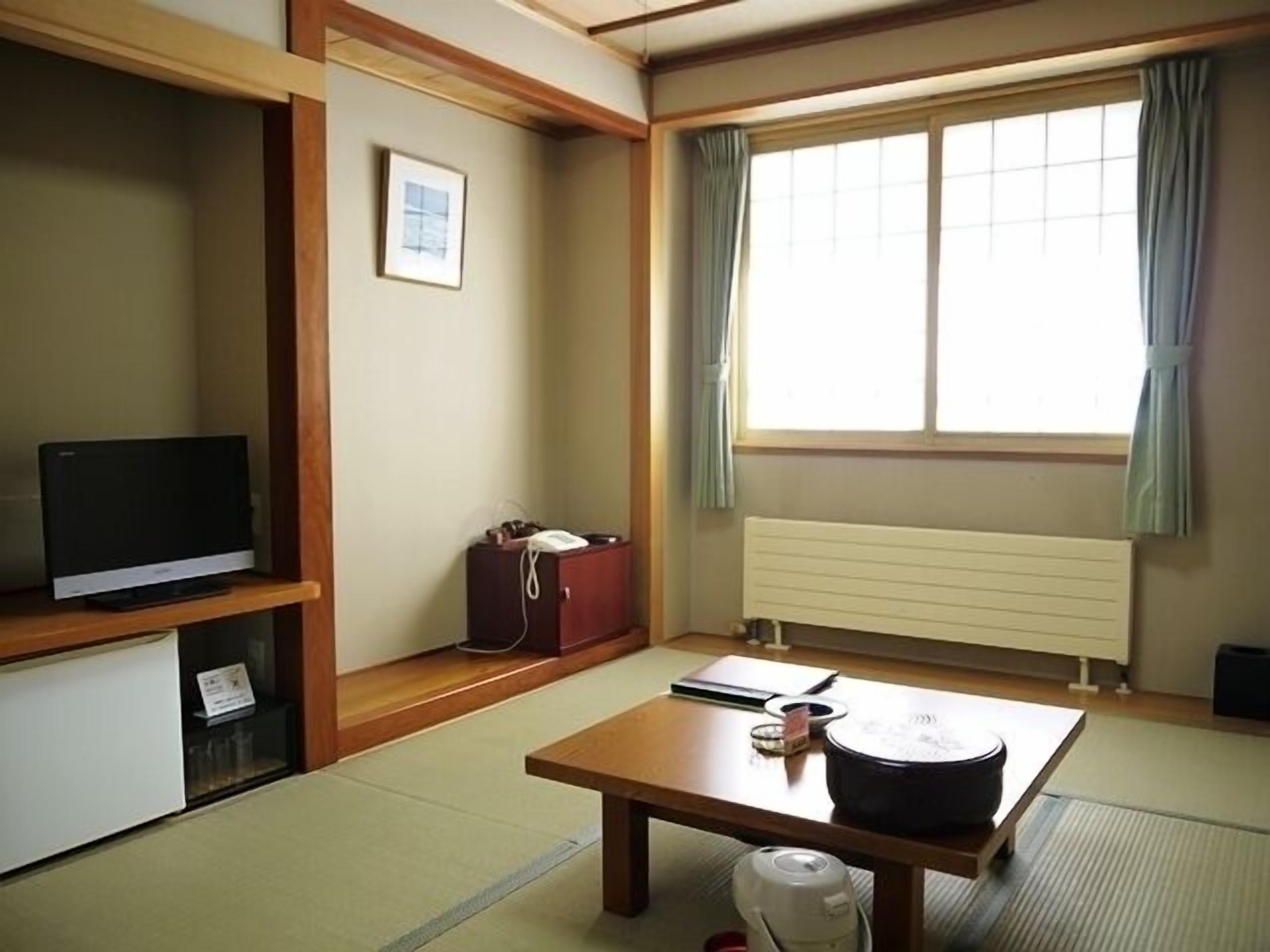 A traditional Japanese room with tatami flooring, a television, a table with a kettle, and a window with curtains.