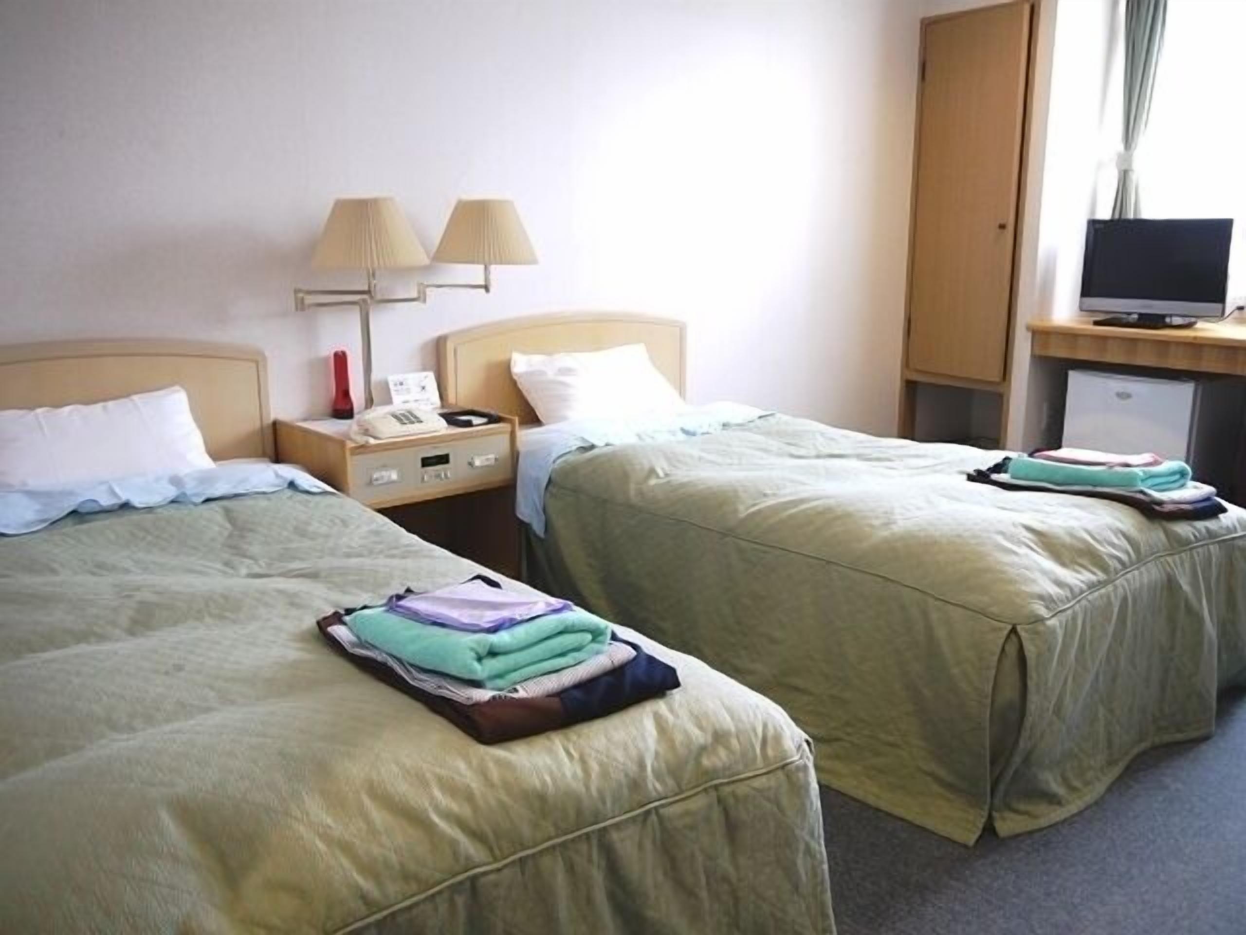 A hotel room with two beds, a desk with a computer, a lamp, and a small refrigerator.