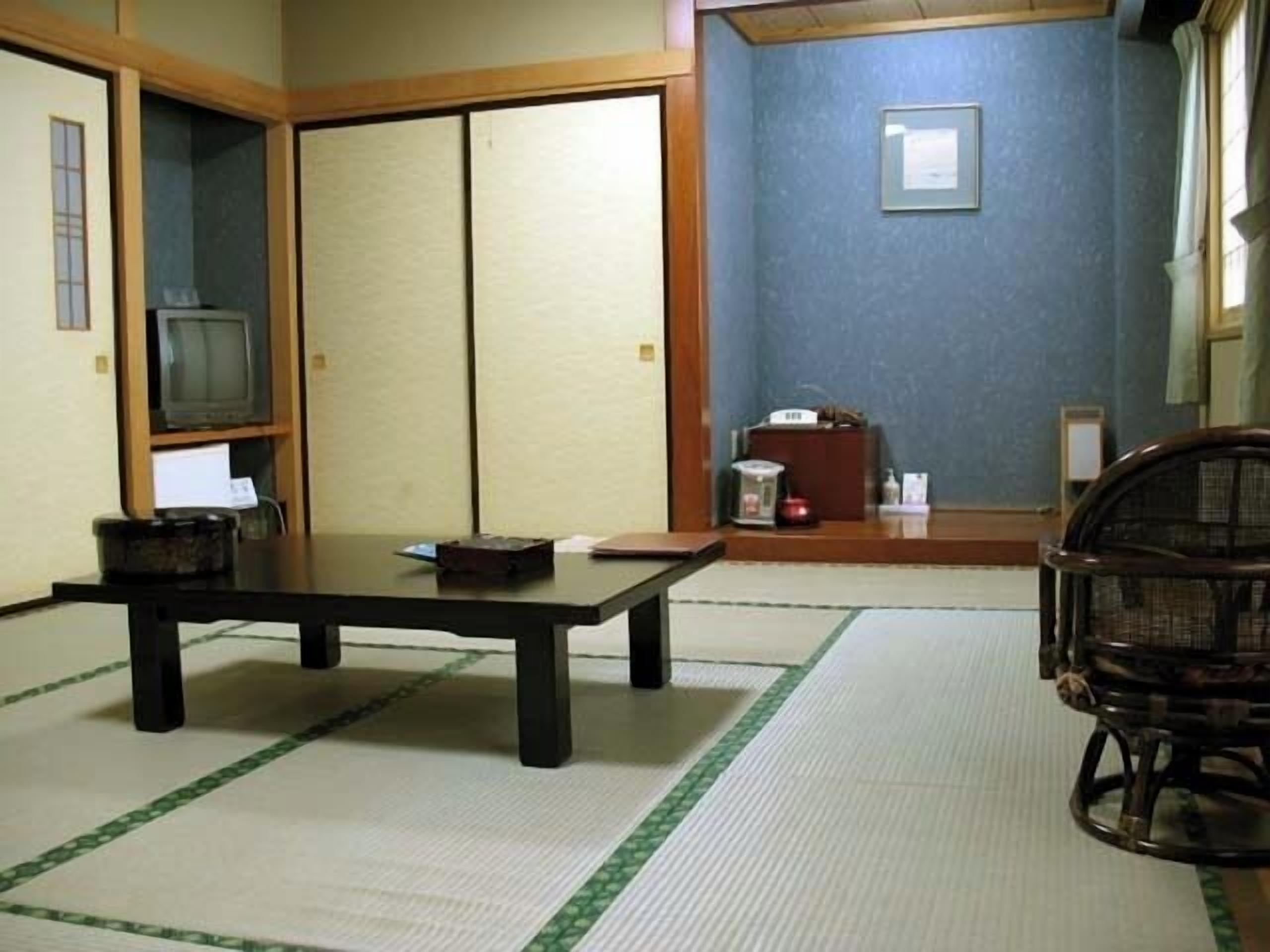 A traditional Japanese room with tatami flooring, a low table, a television, and sliding doors.