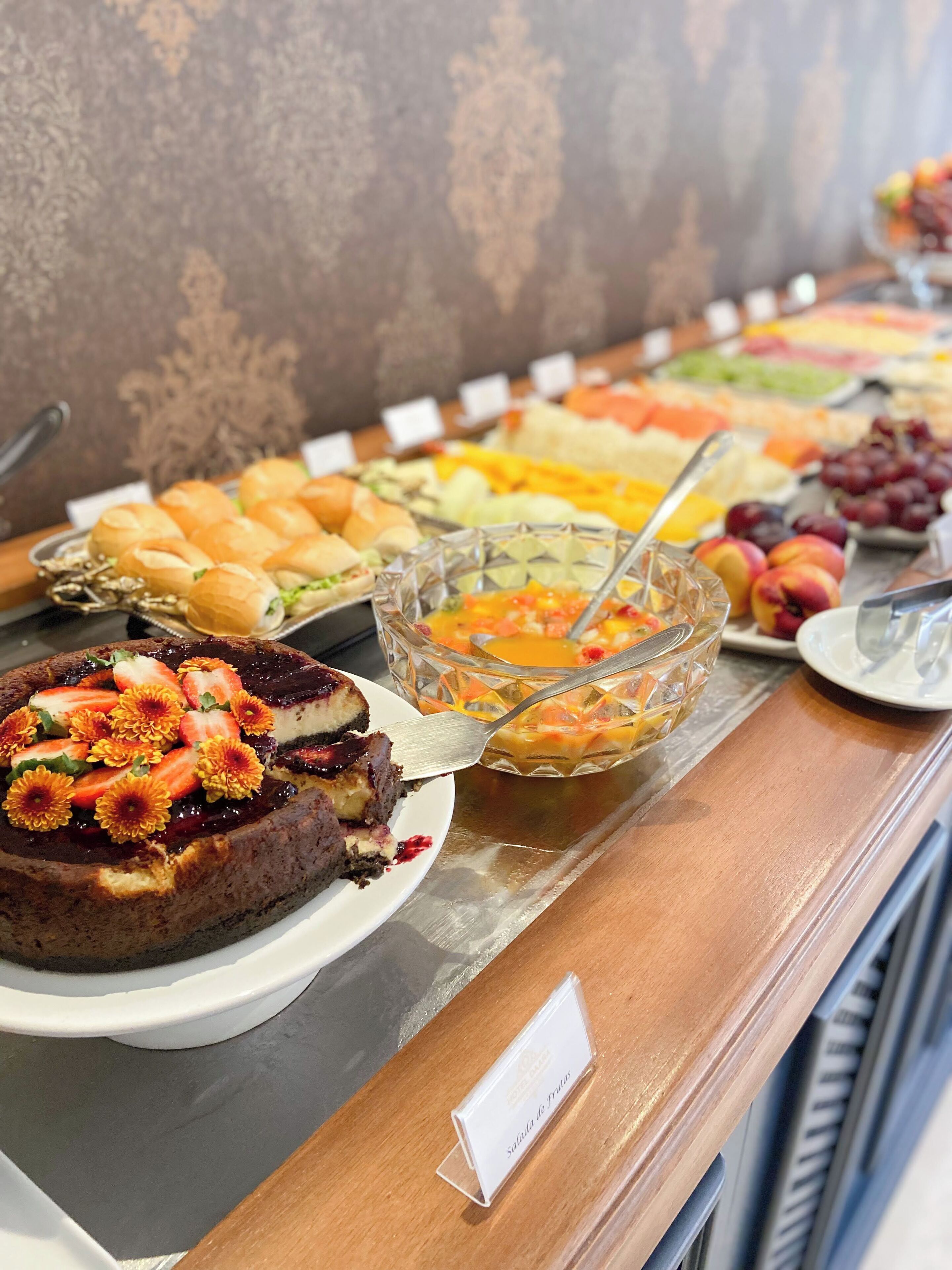 Un bufé con una variedad de comidas, incluyendo un pastel con fresas y flores, y un tazón de ensalada de frutas.