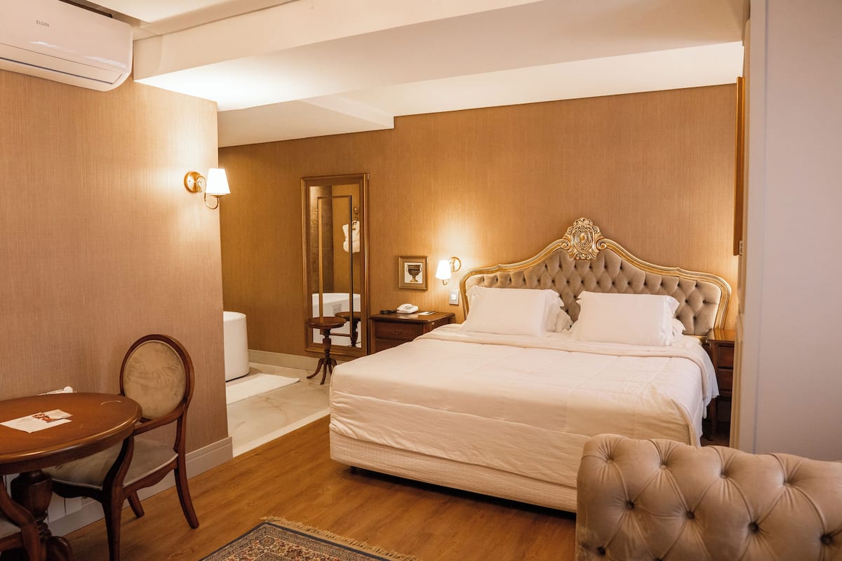 Una camera d'albergo con un letto grande, pavimento in legno, un tavolino con una sedia, un comodino e uno specchio.