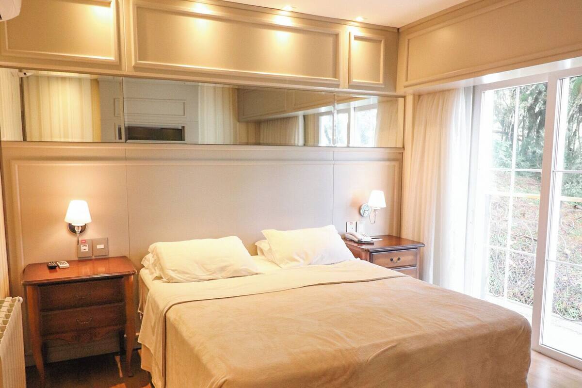 Una camera d'albergo con un grande letto, pavimento in legno, comodini con lampade e vista panoramica da una grande finestra.