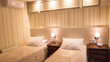 Une chambre d’hôtel avec deux lits simples, des tables de chevet avec des lampes, un climatiseur fixé au mur et un radiateur.