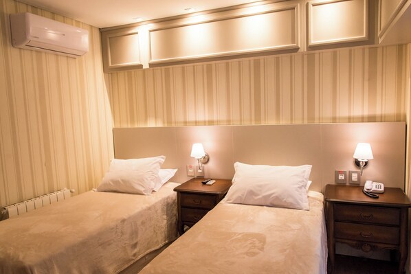 A hotel room with two single beds, bedside tables with lamps, a wall-mounted air conditioner, and a radiator. - Daara Transamerica Collection Gramado (Gramado)