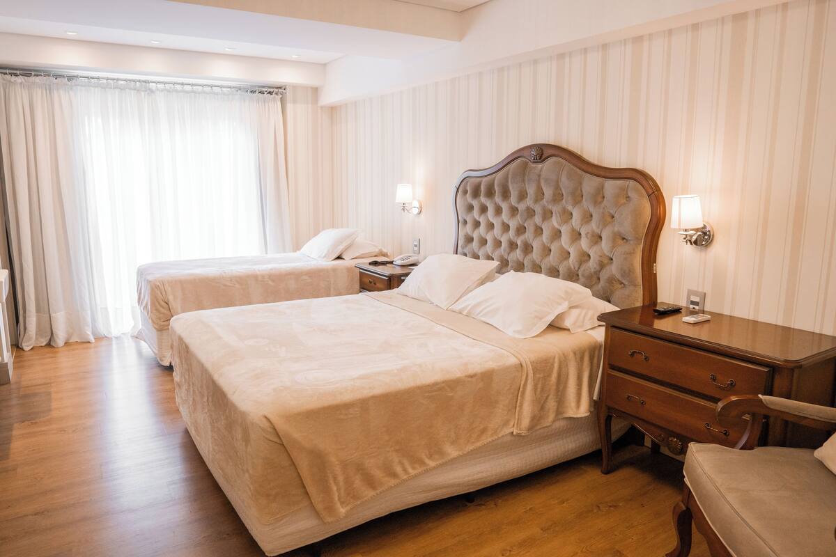 Camera d'albergo con due letti, pavimento in legno, un comodino con una lampada e una sedia.