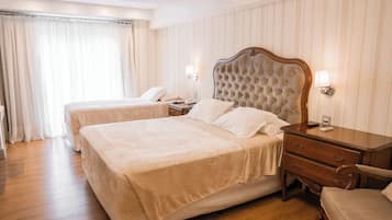 A hotel room with two beds, wooden flooring, a nightstand with a lamp, and a chair.