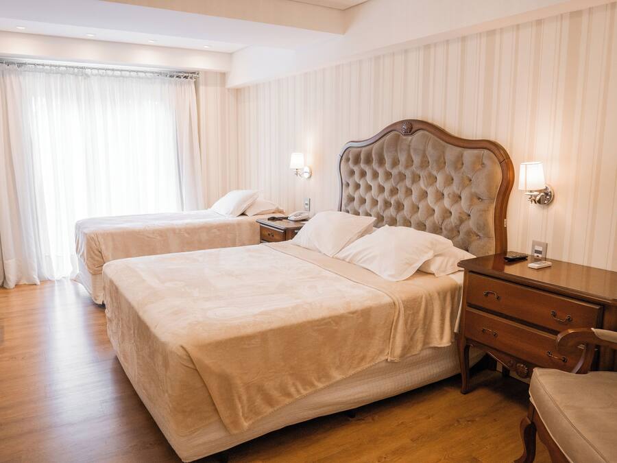 A hotel room with two beds, wooden flooring, a nightstand with a lamp, and a chair.