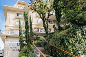 Classic hotel with ornate balconies and lush greenery, offering a charming entrance with a staircase.