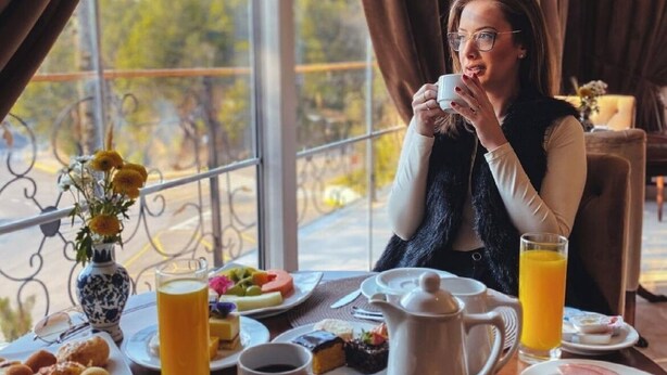A breakfast setting with a table set for two, including plates of food, a coffee pot, a jug of orange juice, and a vase with flowers. - Daara Transamerica Collection Gramado (Gramado)