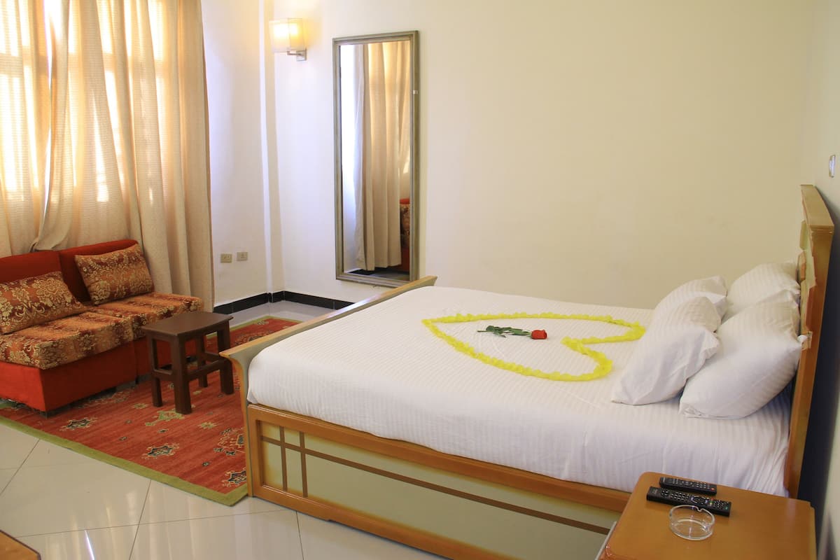 A hotel room with a bed, a sofa, a small table, and a mirror.