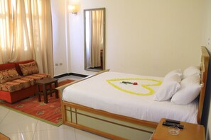 A hotel room with a bed, a sofa, a small table, and a mirror. - Avi Pension (Addis Ababa)