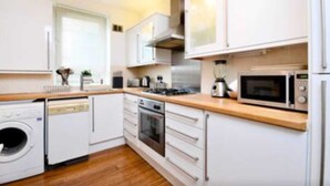 A modern kitchen with white cabinets, a wooden countertop, a built-in oven, a microwave, and a dishwasher. - Stylish 2 Bed Between Camden Town & Primrose Hill (London)