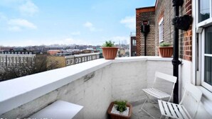 A balcony with a city view, white chairs, and potted plants. - Stylish 2 Bed Between Camden Town & Primrose Hill (London)