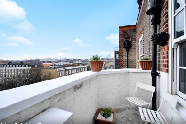 A balcony with a city view, white chairs, and potted plants.