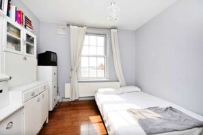 A small, tidy bedroom with a single bed, a white wardrobe, a radiator, and a window with curtains.