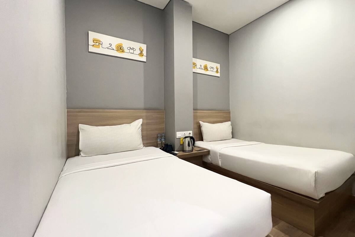 A hotel room with two single beds, a nightstand with a kettle, and two wall-mounted artwork pieces.