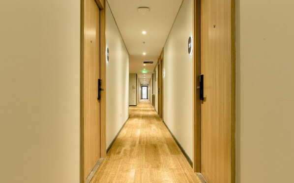 A hotel hallway with wooden doors, a carpeted floor, and a light-colored wall.