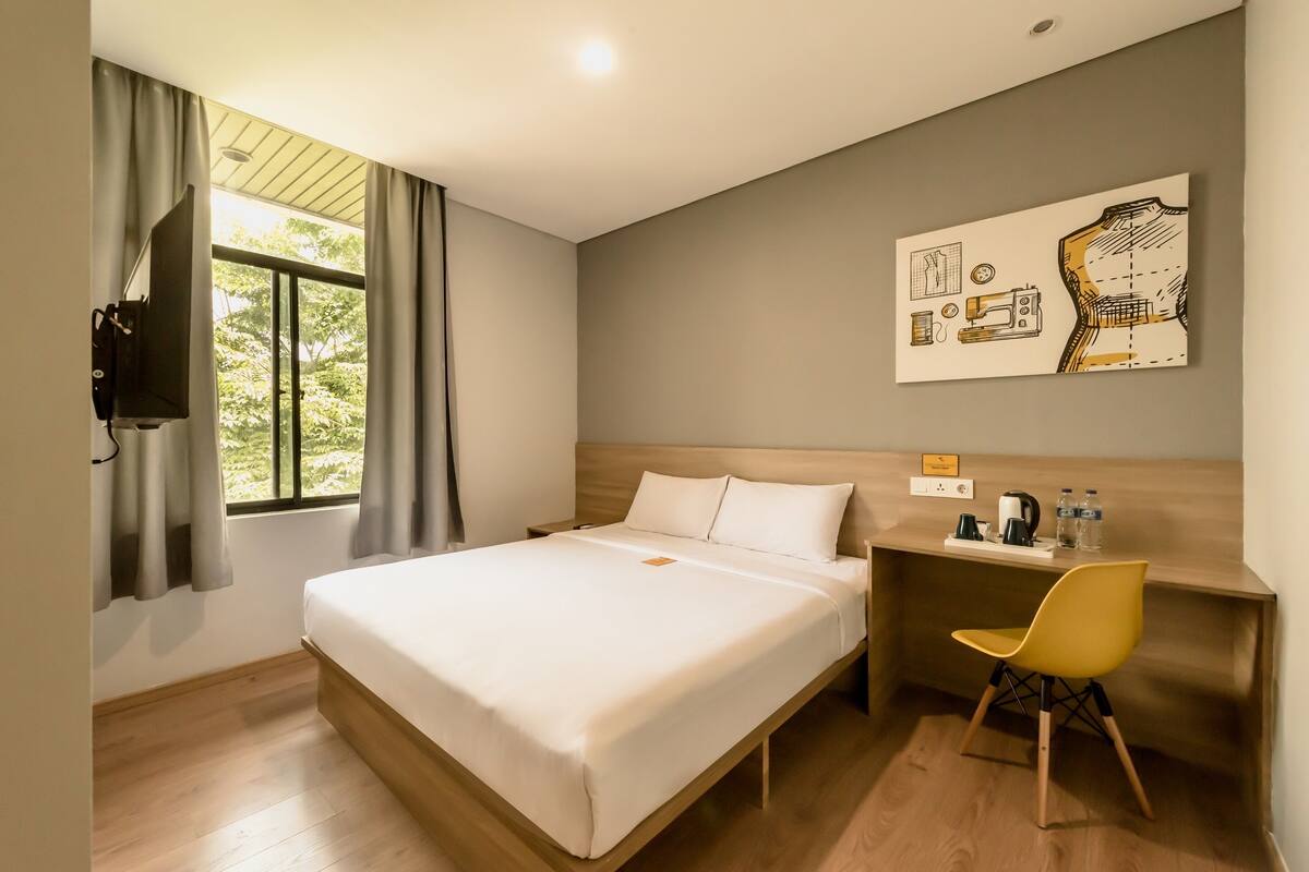 A hotel room with a bed, a desk, a chair, a TV, and a painting on the wall.