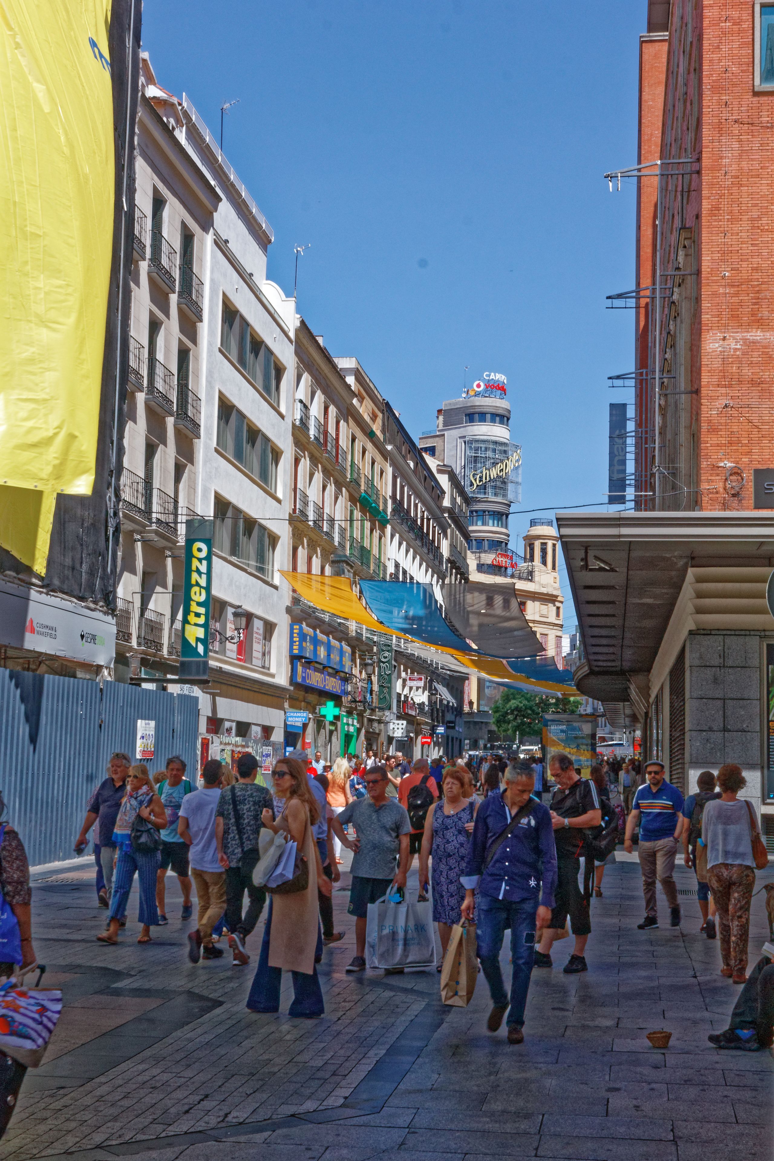 A busy urban street with pedestrians, shops, and a prominent building with a sign.