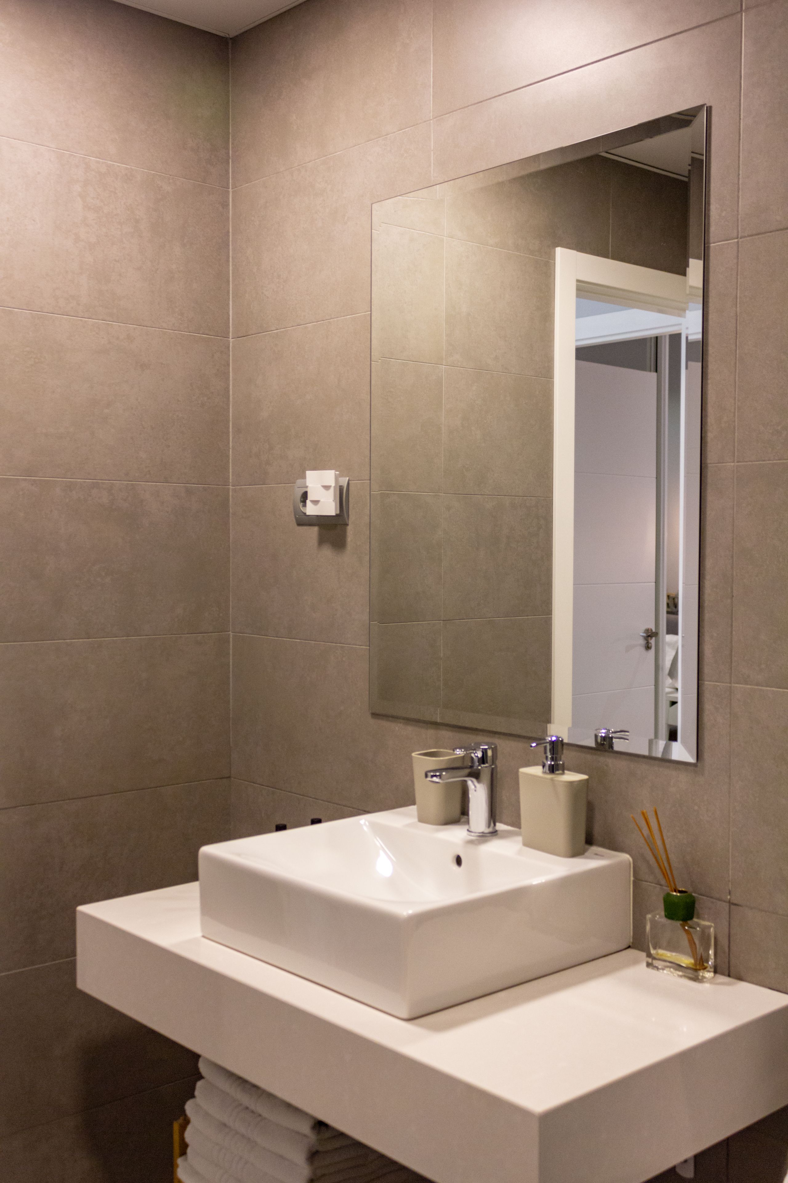A modern bathroom with a large mirror, a white sink, and a towel rack.