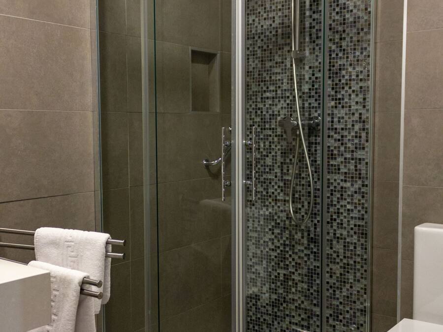 A modern bathroom with a glass-enclosed shower, a white toilet, and a tiled wall.